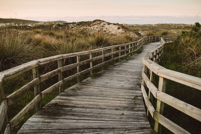 Boardwalk leading towards footbridge against sky