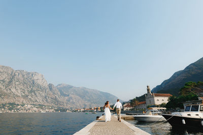 People on sea by mountains against clear sky