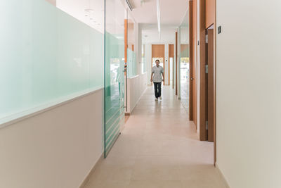 Full body woman in medical uniform looking away while standing in hallway of modern clinic during work