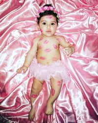 High angle portrait of cute baby girl with lipstick kiss lying on bed at home