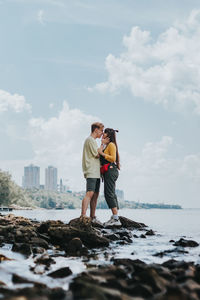 Full length of friends standing at sea shore against sky