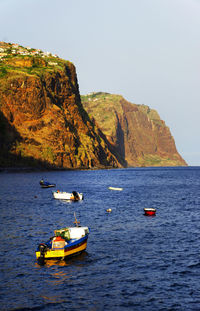 Boats in sea by mountains against clear sky