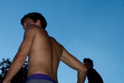 Low angle view of young couple standing against clear blue sky