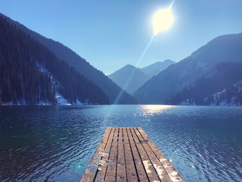 Scenic view of lake by mountains against bright sun