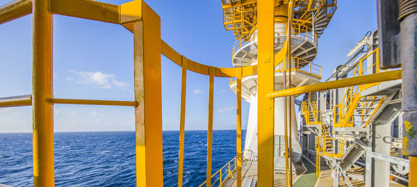 Low angle view of yellow railing by sea against sky