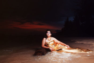 Woman in evening gown sitting on seashore at night