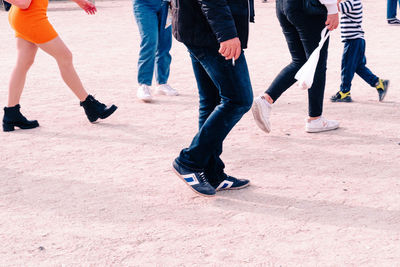 Low section of people walking on sand at beach