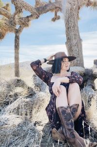 Beautiful woman wearing hat sitting by tree