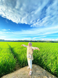 Rear view of woman walking on field against sky