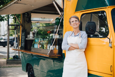 Portrait of mature owner with arms crossed standing against food truck