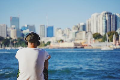 Rear view of man standing by sea against buildings