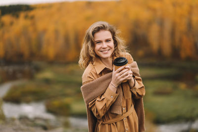 A pretty girl enjoys solitude drinks coffee walks in the autumn forest in nature in fall