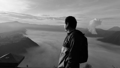 Side view of male hiker looking at cloudscape amidst mountains against sky