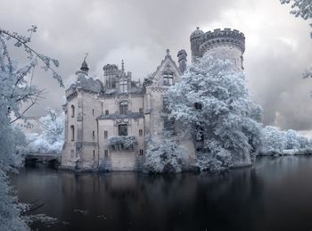 Houses by frozen lake in city against sky