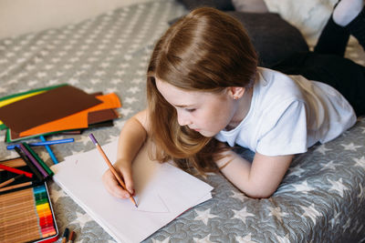 The girl after school plays at home, draws with pencils and felt-tip pens