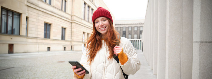 Portrait of young woman standing against building