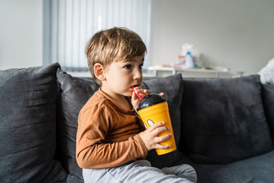 Close-up of boy drinking water on sofa at home