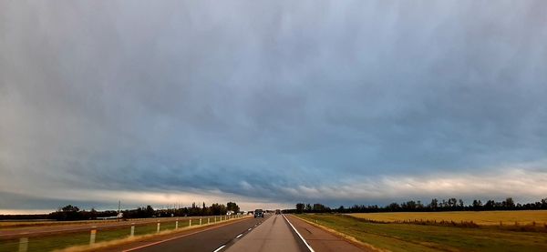 Road passing through field against sky