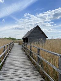 Wooden boardwalk amidst buildings against sky