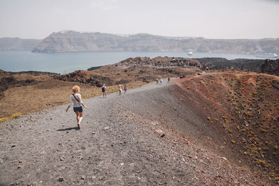 Rear view of woman hiking on dirt road against clear sky