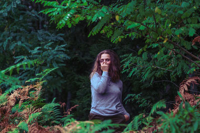 Portrait of woman standing amidst trees at forest