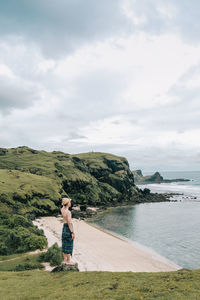 Man standing on cliff at beach against sky