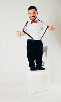 Portrait of man standing on chair against white background