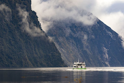 Sailboat sailing on sea by mountains against sky