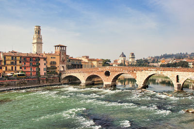 Arch bridge over river by buildings in city against sky