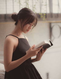 Teenage girl reading book against wall