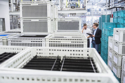 Two men with tablet talking at boxes in factory shop floor