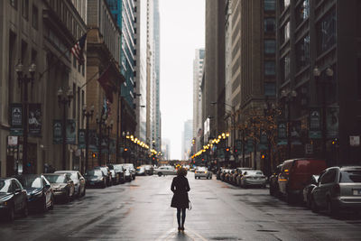 Rear view of man walking on street amidst buildings in city