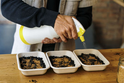 Man spraying water on seeds in tray