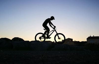 Silhouette man with bicycle against clear sky