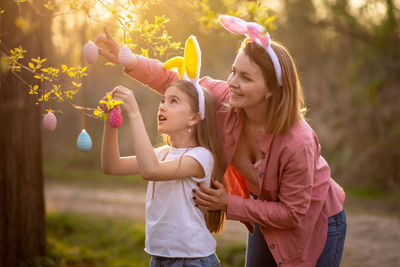 Mother and daughter hanging easter eggs on branch at park