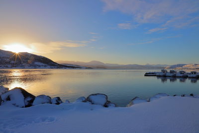 Scenic view of lake by snowcapped mountains against sky during sunset