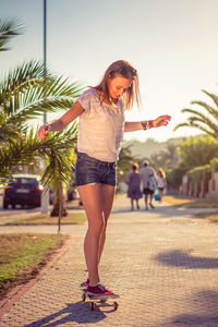 Full length of young woman standing on palm tree in city
