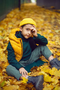 Portrait of a fashionable child boy autumn sitting on a trail in orange leaves in the afternoon