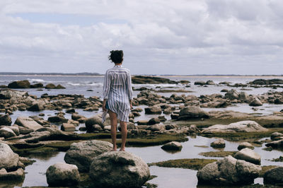 Rear view of woman standing on rock at beach against sky