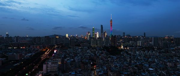 Illuminated buildings in city against cloudy sky