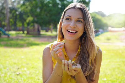 Attractive smiling healthy young woman eating brazil nuts in park on summer