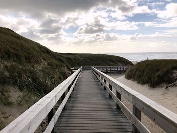 Boardwalk leading towards sea against sky