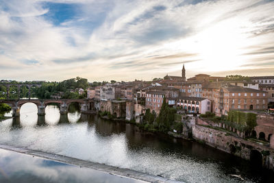 Bridge over river by buildings against sky