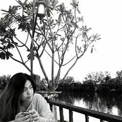 Woman sitting by railing at riverbank against sky