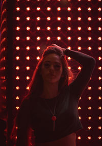 Portrait of young woman standing against illuminated light at night