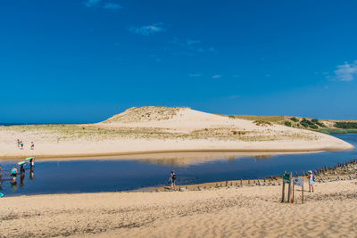 People on sand by river against blue sky