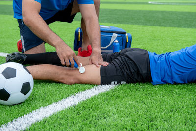 Low section of male physical therapist applying ointment on soccer player leg at field