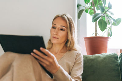 Beautiful blonde young woman artist illustrator drawing on tablet near window at the home