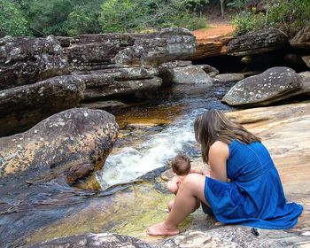 Side view of woman holding daughter by stream in forest