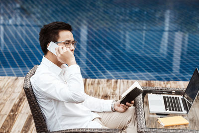 Businessman talking on phone while sitting against swimming pool